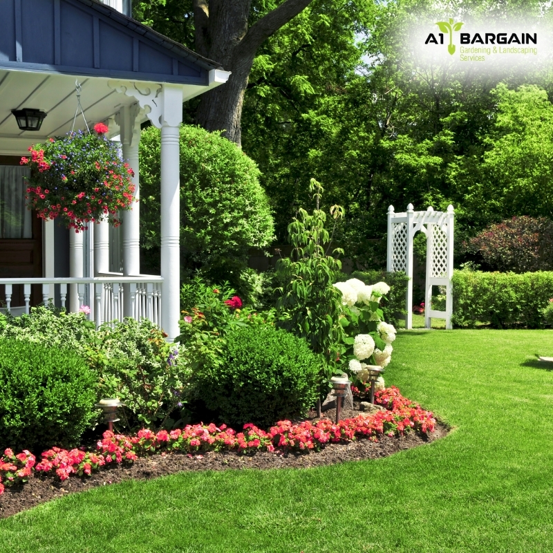 Front yard with a landscaped garden featuring a lush green lawn, flowers, and a white house. Garden landscaping ideas.