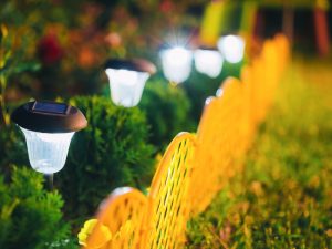 Solar-powered garden lights illuminating an easy garden design with a bright yellow fence and greenery.