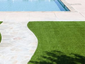 A modern backyard featuring synthetic turf for backyards, a sparkling pool, and lush greenery, perfect for outdoor relaxation and entertaining.