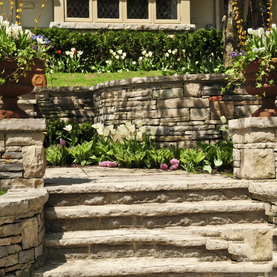 Retaining Walls Sydney: Stone retaining wall with stairs and landscaping, showcasing professional installation.