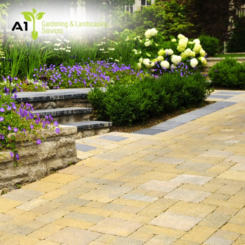 Beautifully landscaped garden with vibrant flowers, green shrubs, and stone paving in Bayview leading to steps, featuring a logo overlay.
