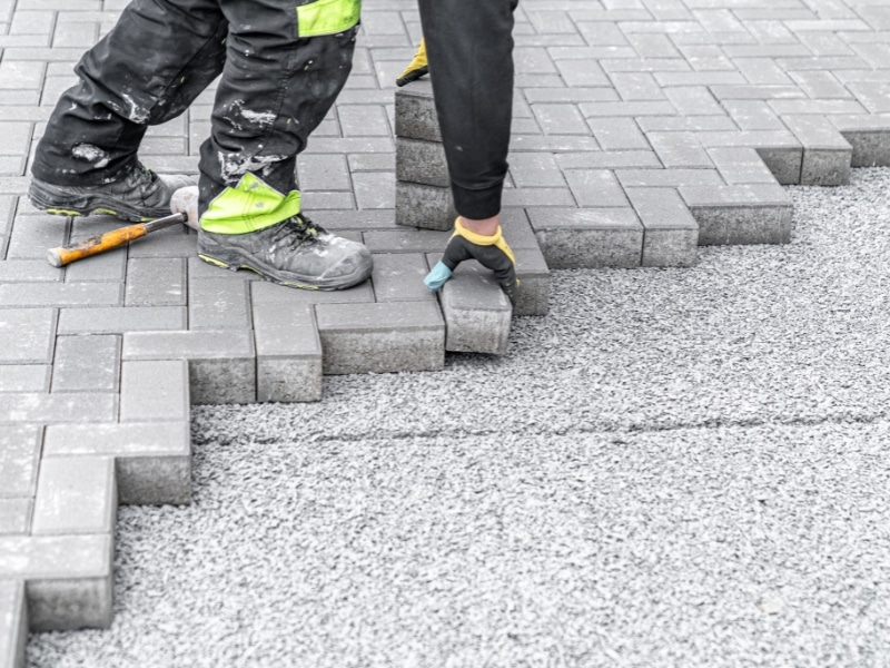 Laying natural stone paving bricks on prepared gravel driveway surface.